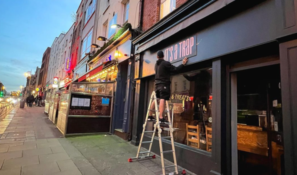 man on ladder adjusting a sign which reads "its a trap" on a black shop front