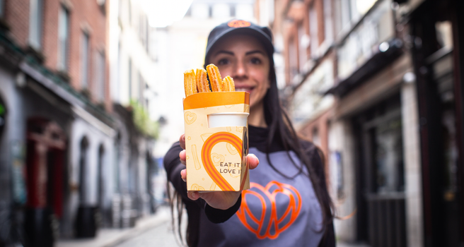 woman in a Sweet Churro apron and cap holding a cardboard container of churros