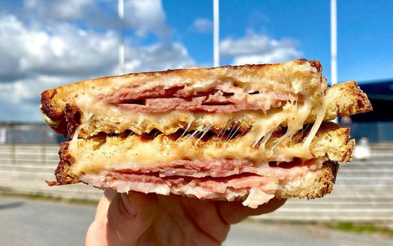 person holding up a ham and cheese toastie with blue sky in the background