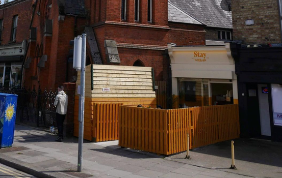white cafe with "stay with us" painted above the door, and yellow wooden fencing surrounding it
