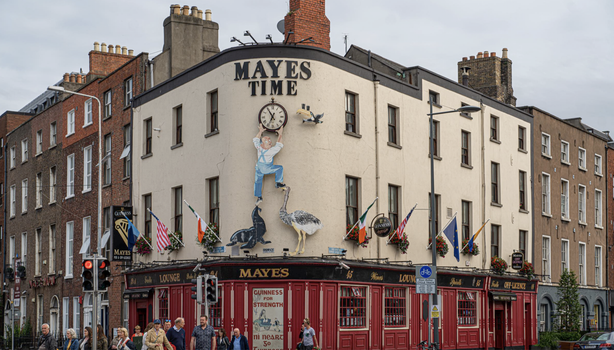 exterior of Mayes Pub in Dublin - a red pub with white building above, a sign reads "Mayes Time" with a large clock below