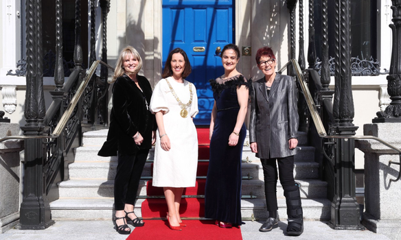 Mary Aiken, the Lord Mayor of Dublin, Kellie Harrington and Ailbhe Smyth standing and smiling on steps outside a building with a blue door and red carpet leading up to it.