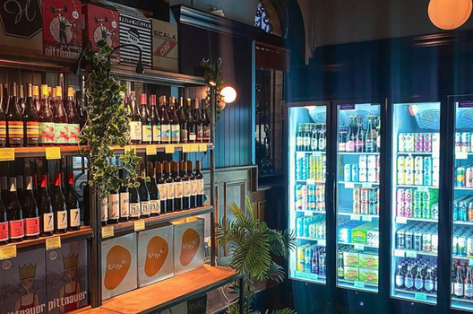 interior of an off licence with shelves filled with wine bottles and a fridge full of colourful cans