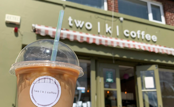 iced coffee cup with shop front of a cafe in the background, sign reads "two | k | coffee"