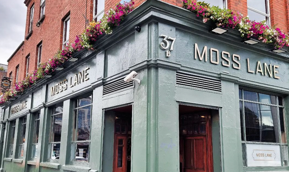 exterior of moss lane pub with green paint and hanging flower baskets