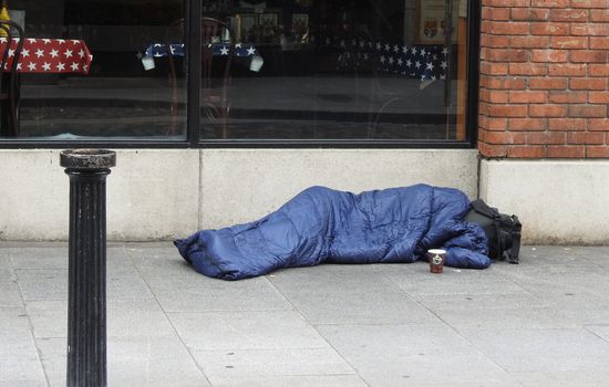 person sleeping in sleeping back with face covered, on the side of a street in Dublin